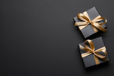Photo of Shiny gift box with golden bow on black background, flat lay. Space for text