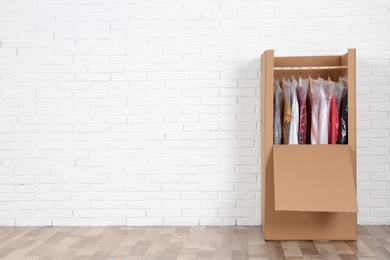Photo of Wardrobe box with clothes against brick wall indoors. Space for text