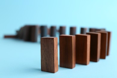 Photo of Row of wooden domino tiles on light blue background, closeup