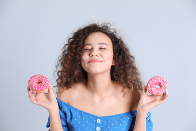 Beautiful African-American woman with donuts on light grey background