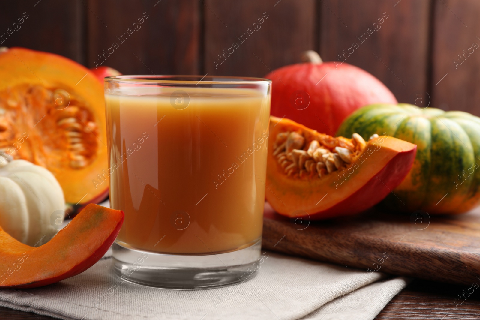 Photo of Tasty pumpkin juice in glass and different pumpkins on wooden table