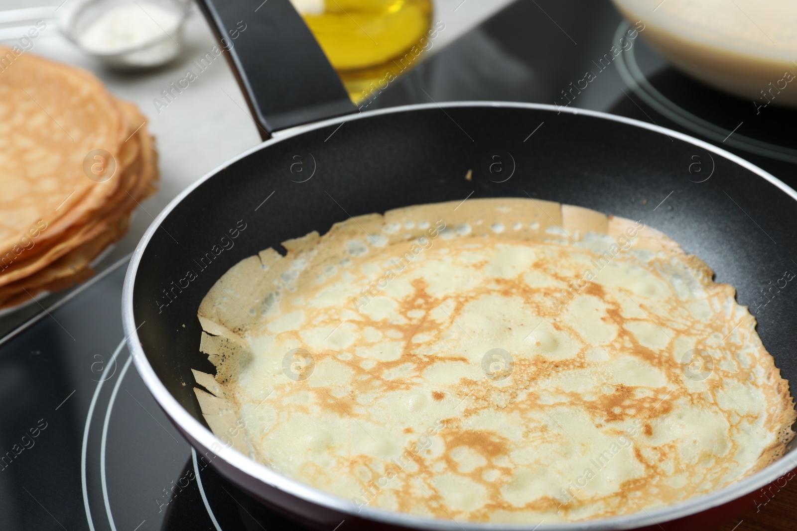 Photo of Delicious thin pancake in frying pan on induction stove, closeup