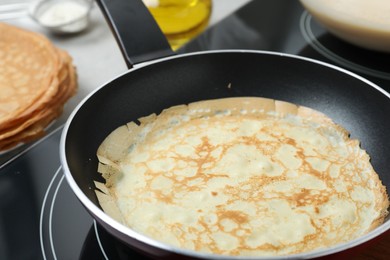 Delicious thin pancake in frying pan on induction stove, closeup