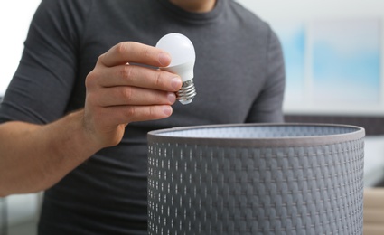 Man changing light bulb in lamp indoors, closeup