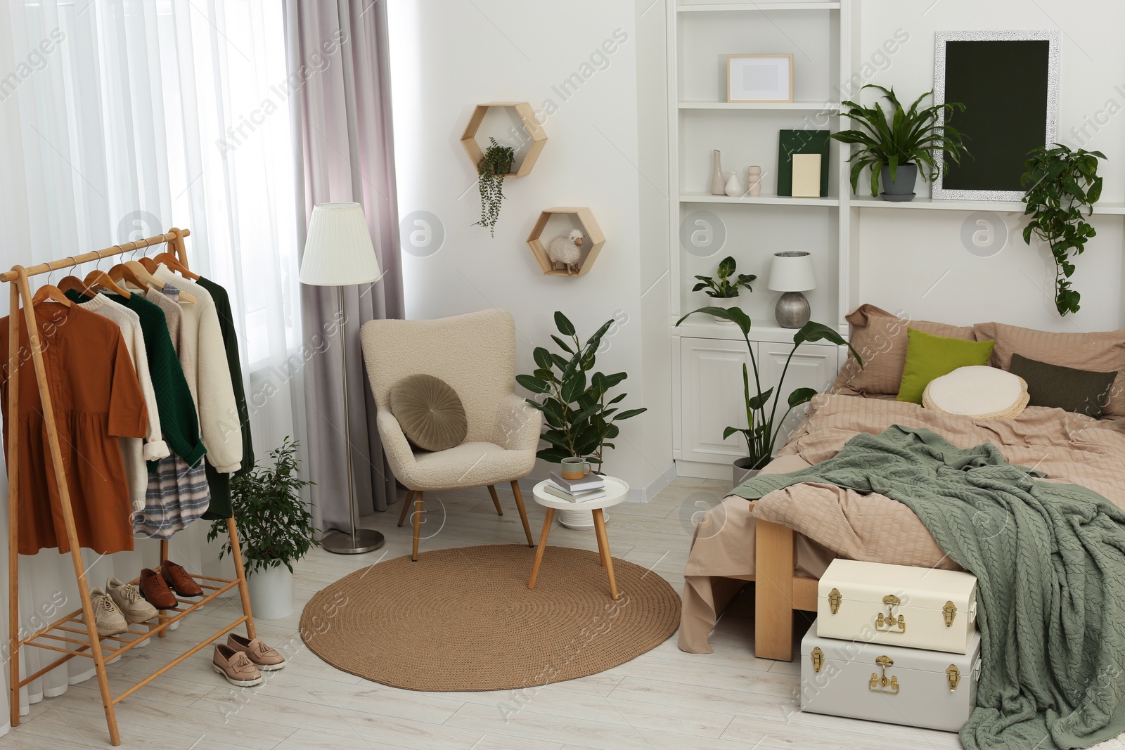 Photo of Stylish bedroom with comfortable bed, clothes rack and different houseplants. Interior design