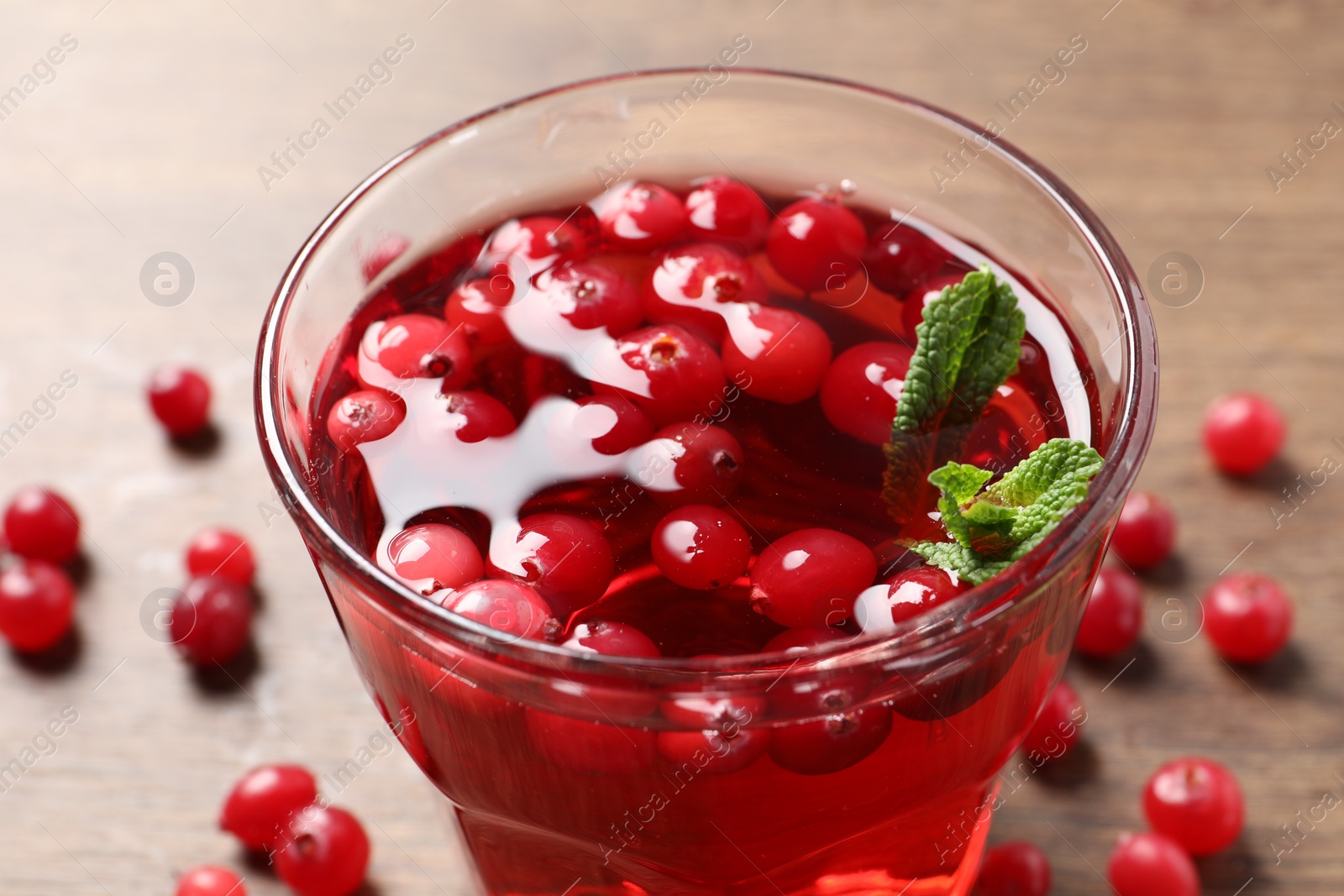 Photo of Tasty cranberry juice in glass and fresh berries on wooden table, closeup