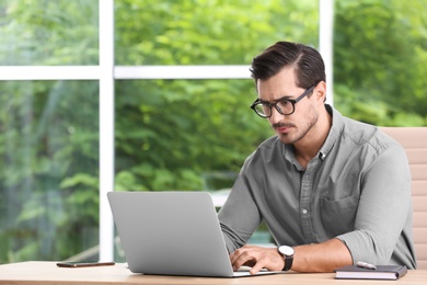 Photo of Handsome young man working with laptop at table in office