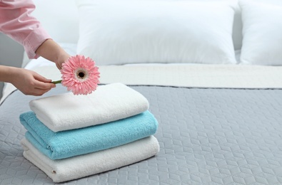 Woman putting flower on stack of clean towels in bedroom. Space for text