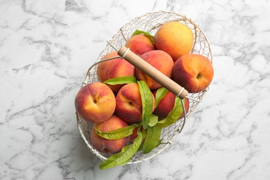 Photo of Fresh sweet peaches in metal basket on white marble table, top view