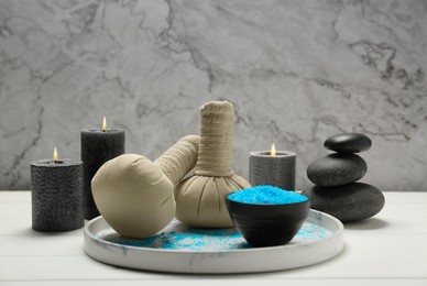 Spa composition with herbal bags and burning candles on white wooden table