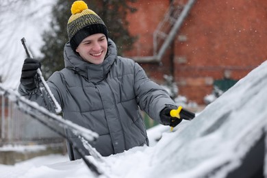 Photo of Man cleaning snow from car windshield outdoors