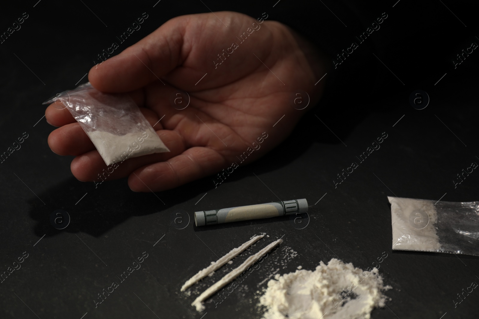 Photo of Drug addiction. Man with cocaine and rolled dollar banknote at dark table, closeup
