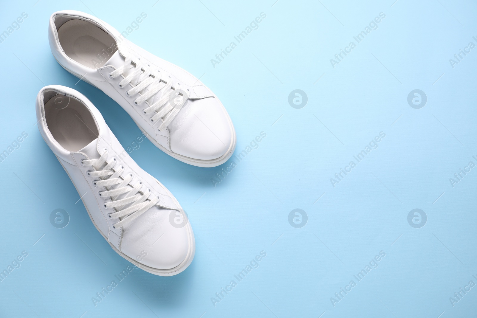 Photo of Pair of stylish white sneakers on light blue background, top view. Space for text