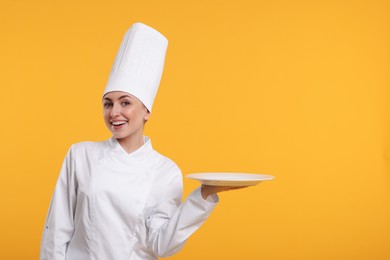 Photo of Happy professional confectioner in uniform holding empty plate on yellow background. Space for text