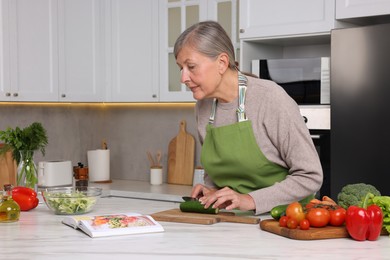 Photo of Senior woman cooking by recipe book in kitchen