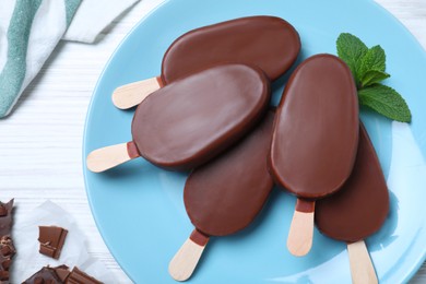 Photo of Glazed ice cream bars with fresh mint and chocolate on white wooden table, flat lay