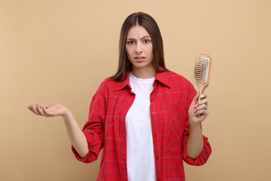 Emotional woman holding brush with lost hair on beige background. Alopecia problem