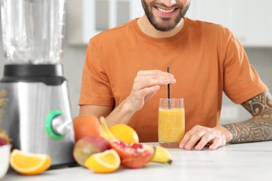 Photo of Man with delicious smoothie at white marble table in kitchen, closeup