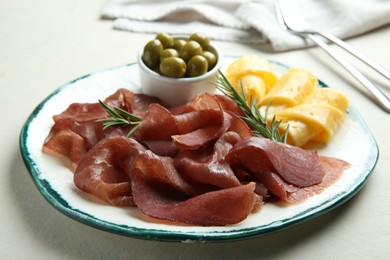 Photo of Delicious bresaola, cheese, olives and rosemary on light table, closeup