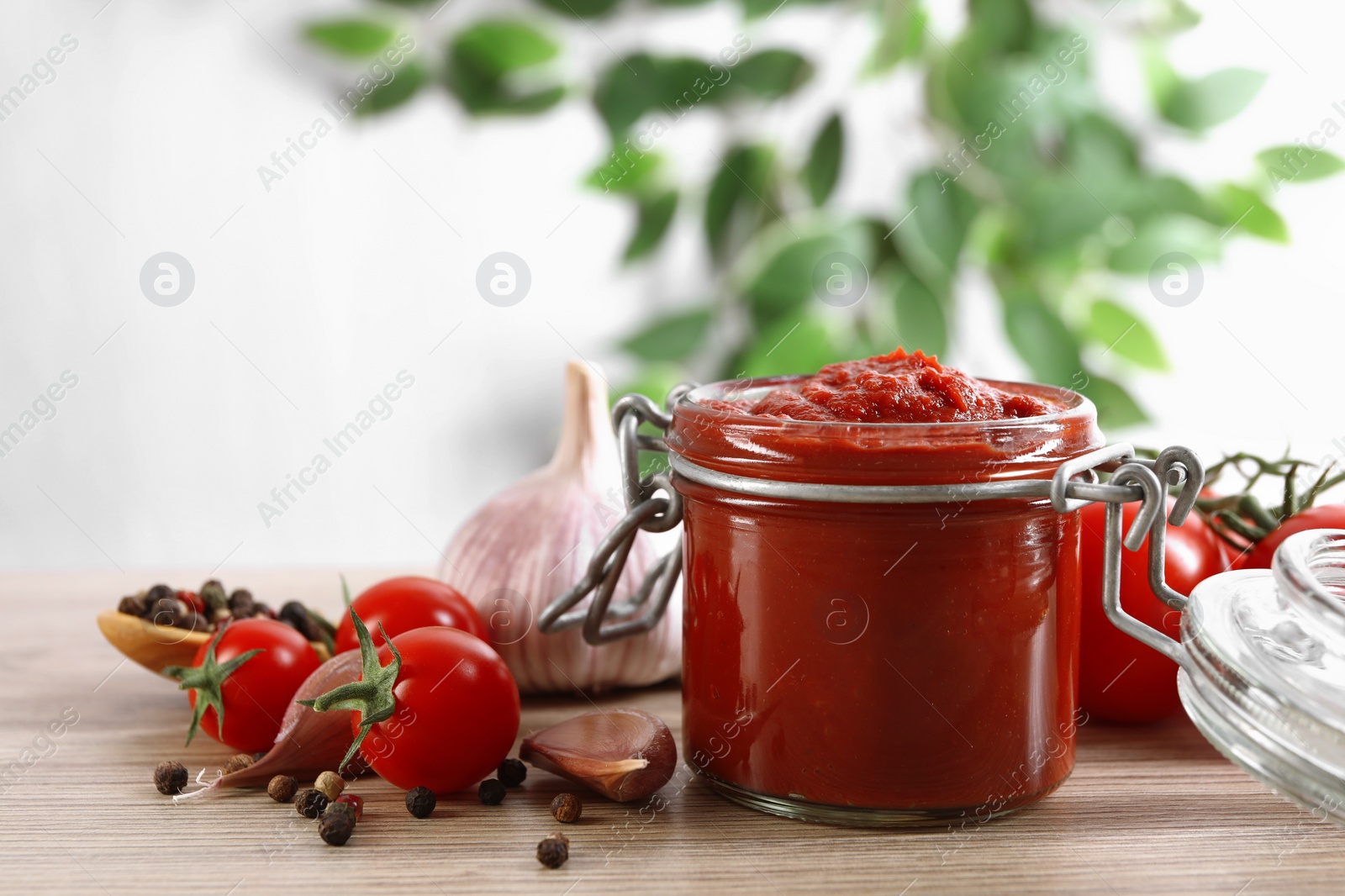 Photo of Jar of tasty tomato paste and ingredients on wooden table, space for text