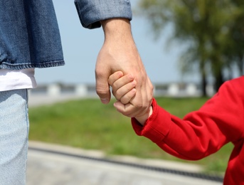 Photo of Little child holding hands with his father  outdoors, closeup. Family weekend