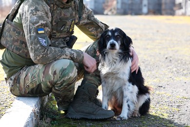 Photo of Ukrainian soldier with stray dog outdoors on sunny day, closeup
