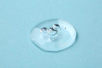 Photo of Drop of cosmetic serum on light blue background, closeup