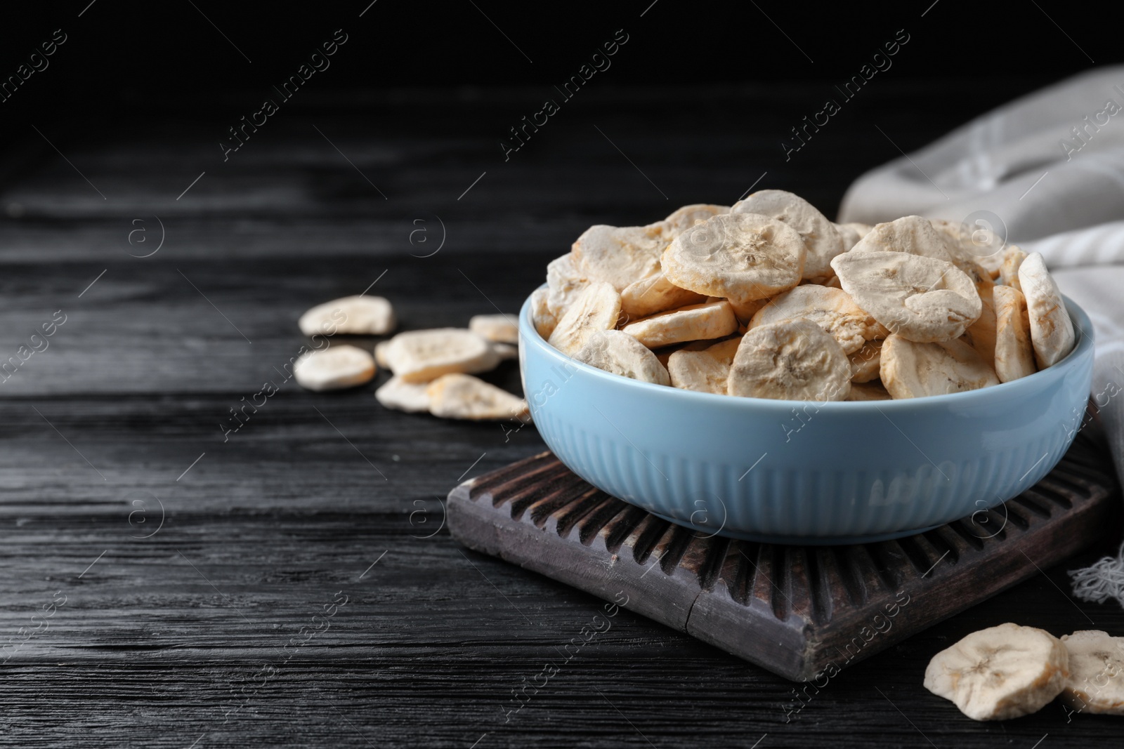 Photo of Bowl and dried banana slices on black wooden table. Space for text