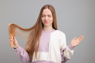 Photo of Emotional woman brushing her hair on light grey background. Alopecia problem