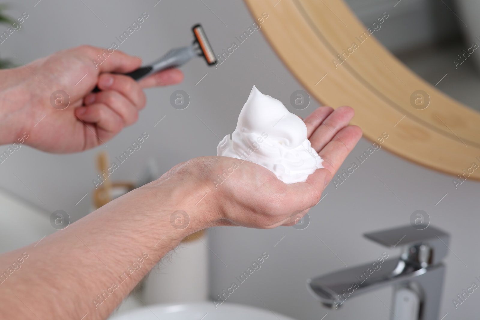 Photo of Man holding shaving foam and razor in bathroom, closeup