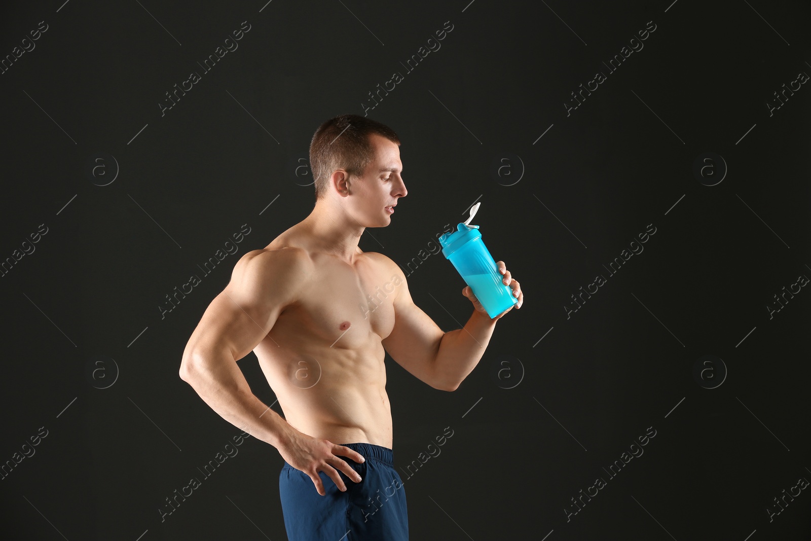 Photo of Athletic young man with protein shake on black background