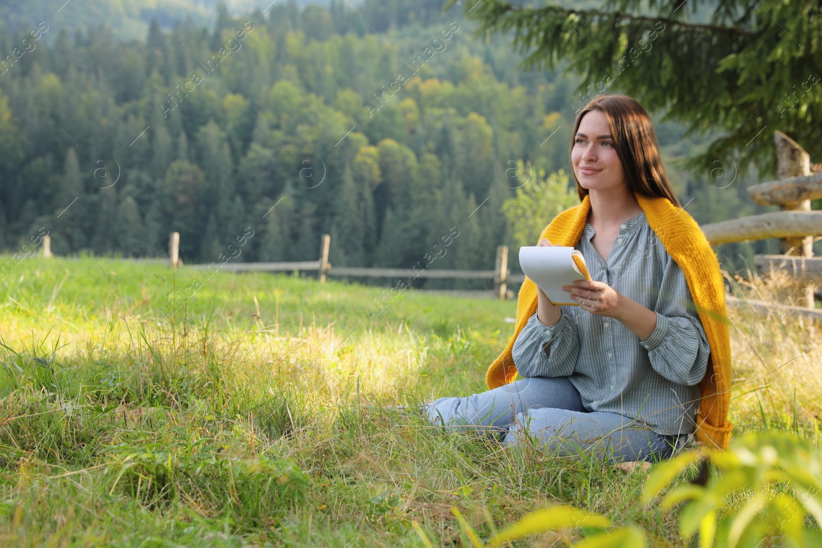 Photo of Beautiful young woman drawing with pencil in notepad on green grass