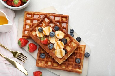 Photo of Delicious Belgian waffles with banana, berries and caramel sauce on light marble table, flat lay