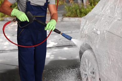 Photo of Worker washing auto with high pressure water jet at outdoor car wash, closeup