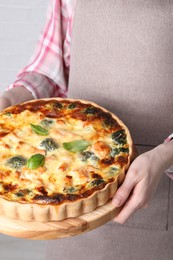 Photo of Woman holding delicious homemade quiche with salmon and broccoli on light background, closeup