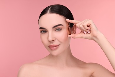 Photo of Beautiful young woman holding skincare ampoule on pink background