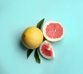 Photo of Fresh cut and whole pomelo fruits with leaves on turquoise background, flat lay