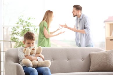 Little unhappy boy sitting on sofa while parents arguing at home