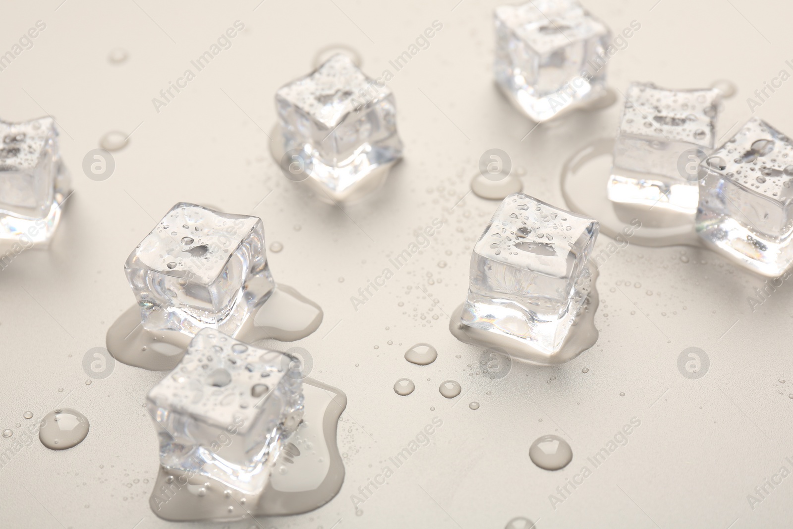 Photo of Melting ice cubes and water drops on light grey background, closeup
