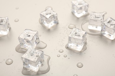 Melting ice cubes and water drops on light grey background, closeup