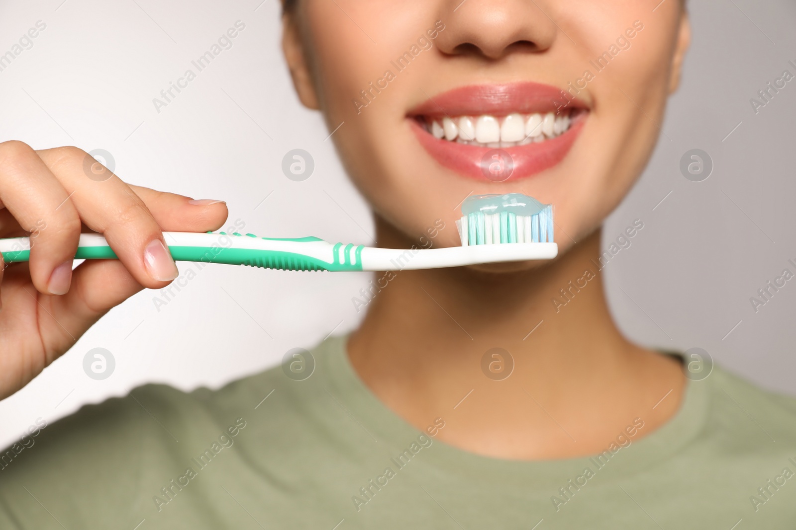Photo of Woman holding toothbrush with paste on light background, closeup