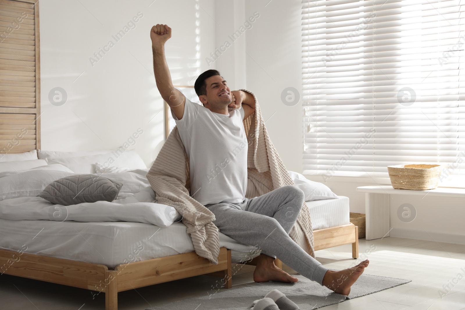 Photo of Happy man covered with beige plaid stretching in bedroom