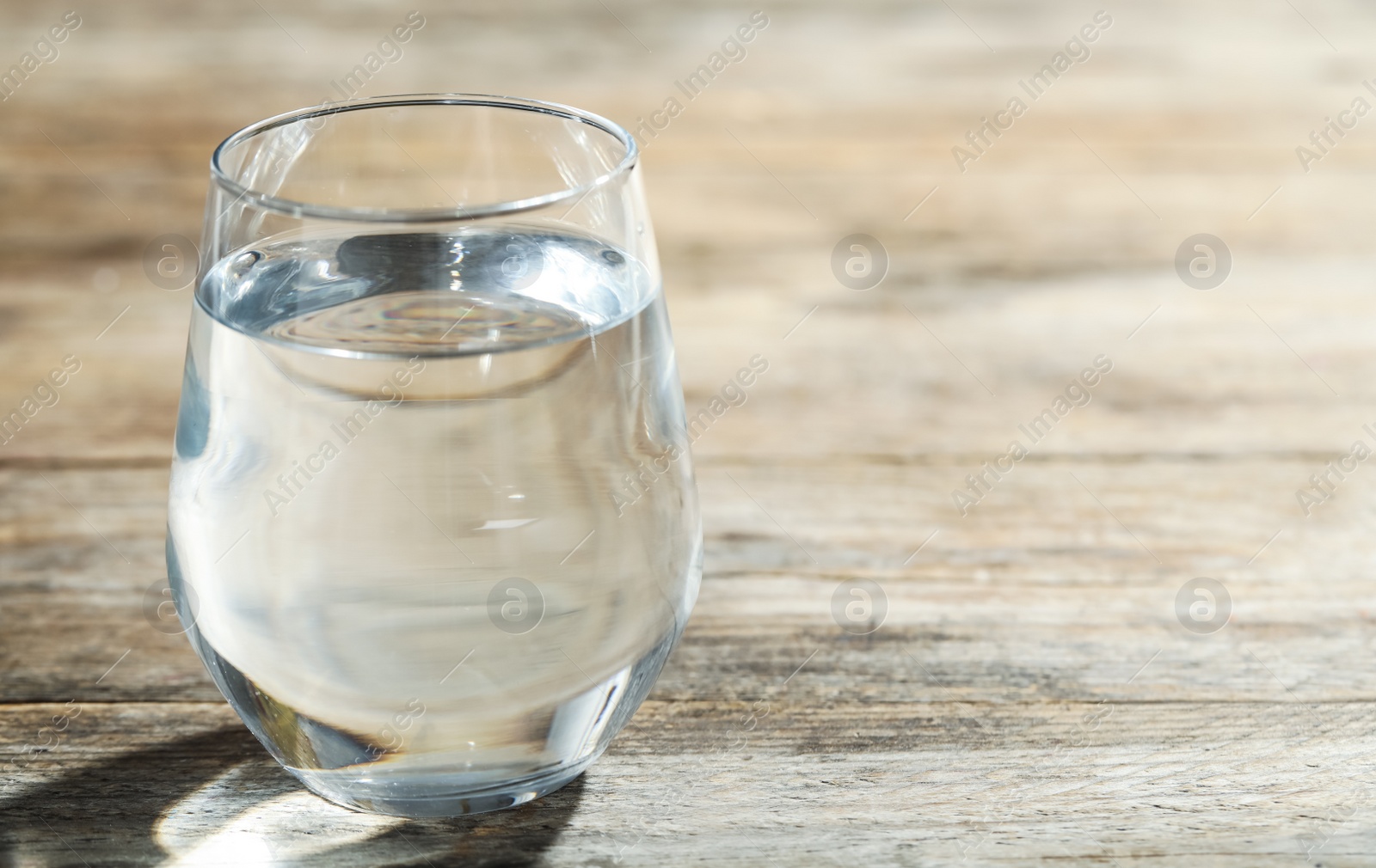 Photo of Glass of water on wooden table, closeup with space for text. Refreshing drink