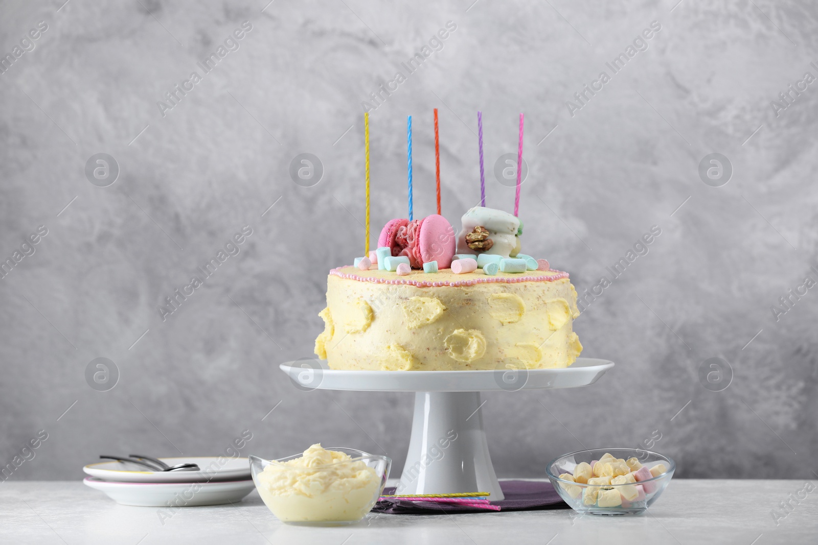 Photo of Delicious cake decorated with macarons, marshmallows and candles served on white table against grey background