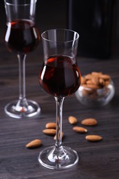 Photo of Liqueur glasses with tasty amaretto and almonds on wooden table, closeup