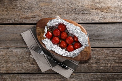 Photo of Aluminum foil with delicious baked tomatoes on wooden table, top view