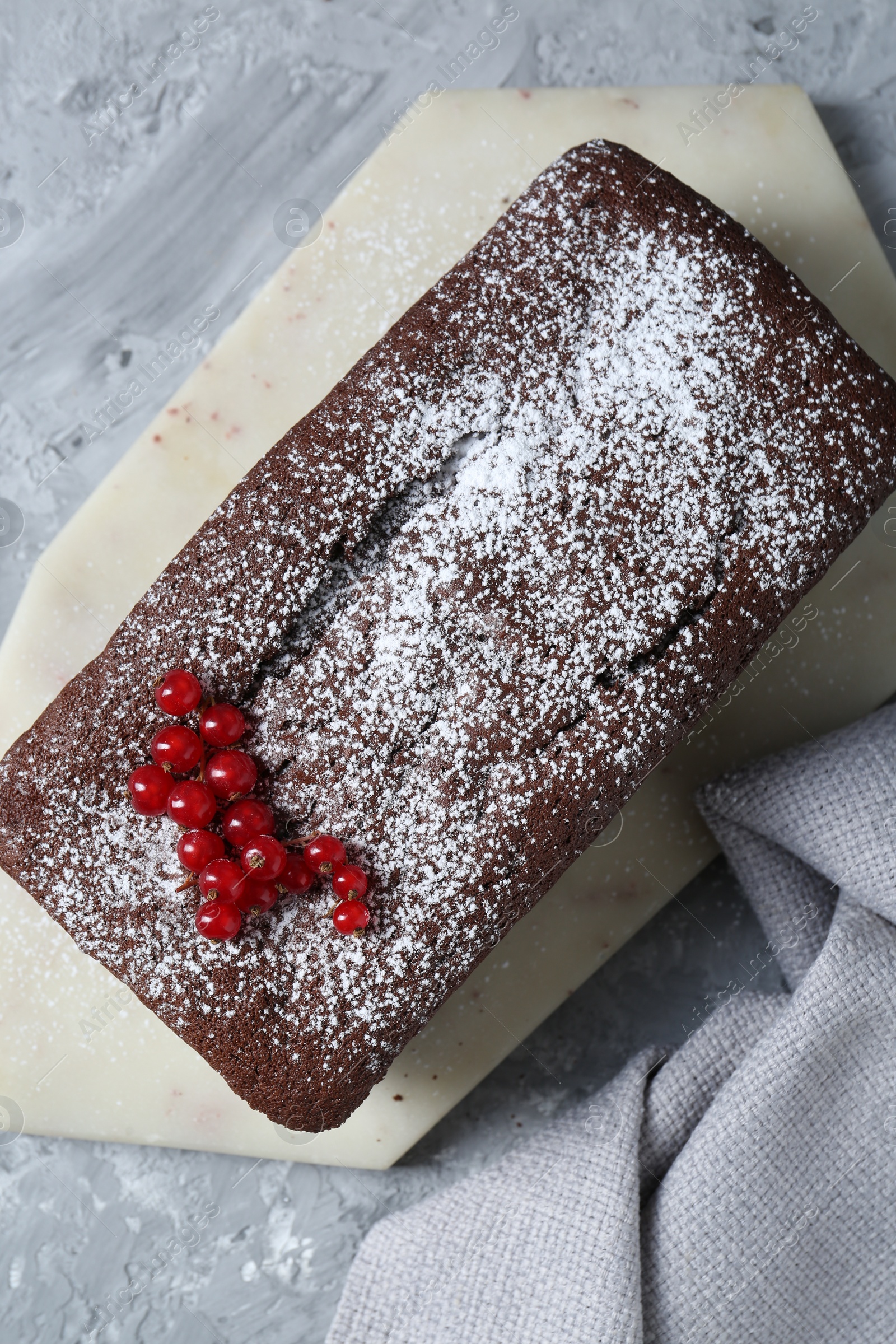 Photo of Tasty chocolate sponge cake with powdered sugar and currant on light grey textured table, top view