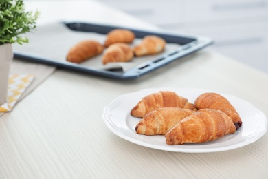 Plate with freshly baked croissants on table in kitchen