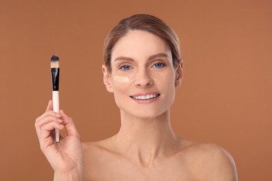Woman with swatch of foundation and makeup brush against brown background