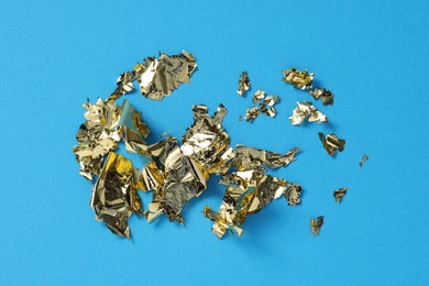Photo of Pieces of edible gold leaf on light blue background, flat lay